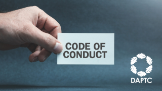 Hand holding card with Code of Conduct printed on it against a dark grey background